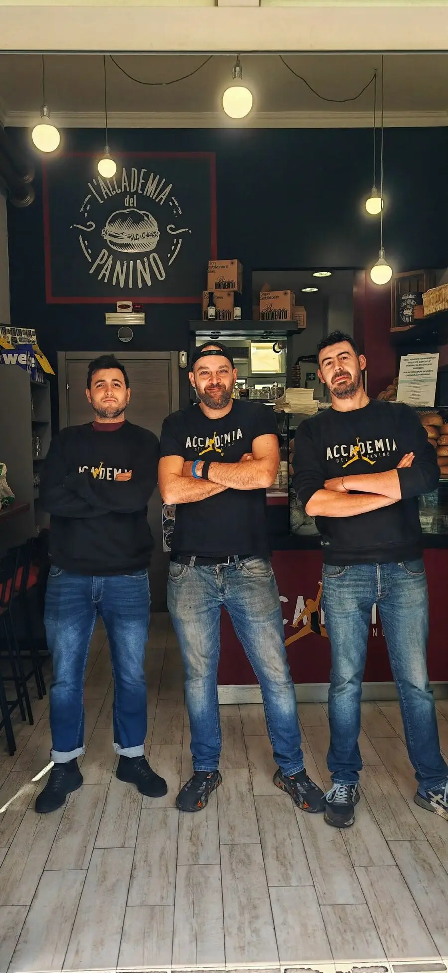 The Accademia del Panino staff in front of the counter, under the logo painted on the wall